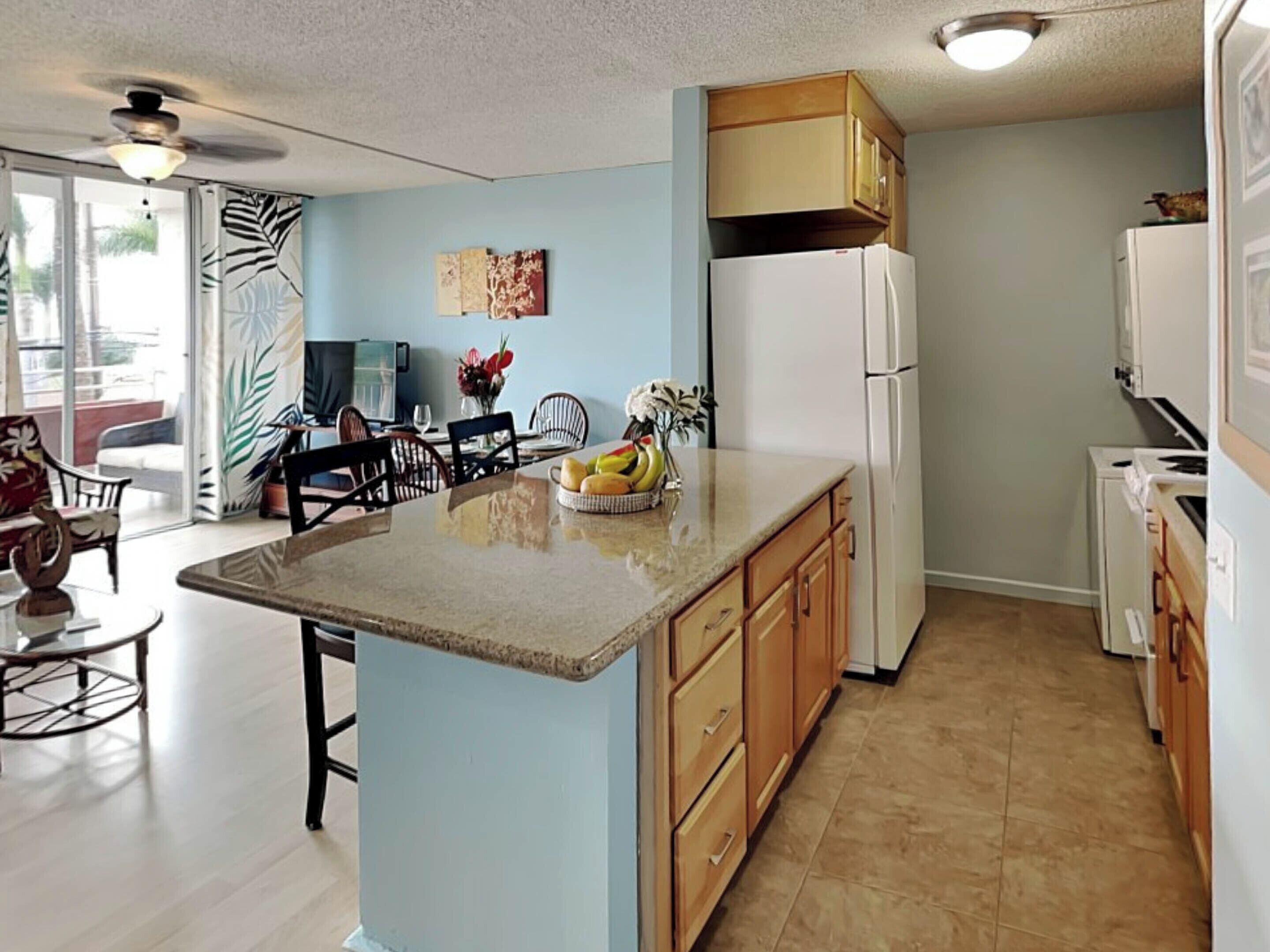 A modern kitchen with a central island, wooden cabinets, and a refrigerator.