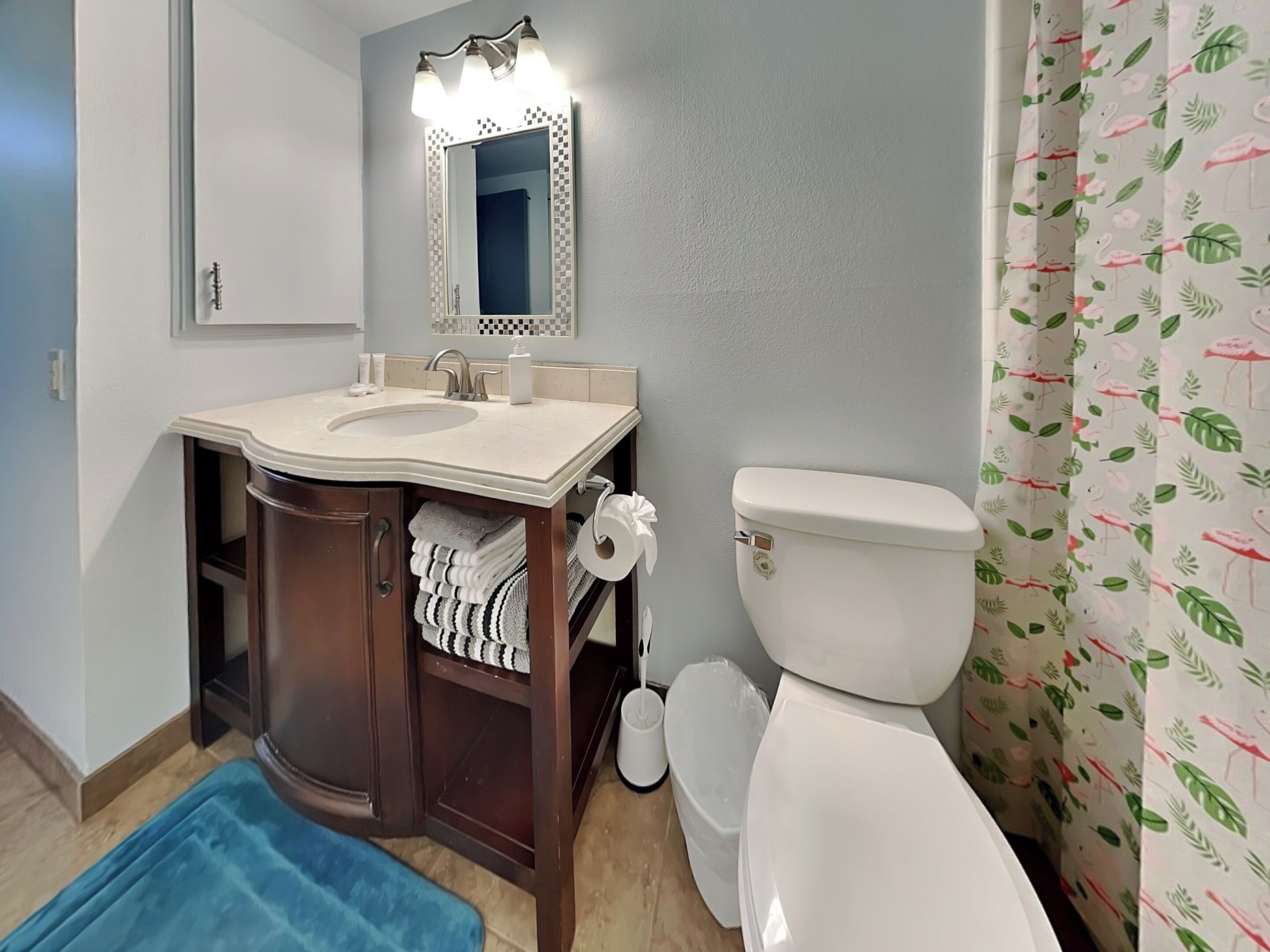 A bathroom with a sink, mirror, toilet, and blue bath mat.