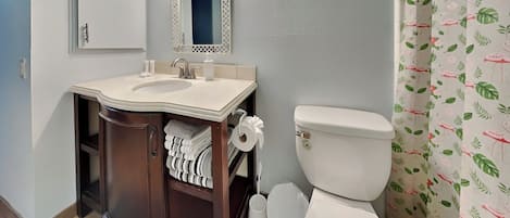 A bathroom with a sink, mirror, toilet, and blue bath mat.