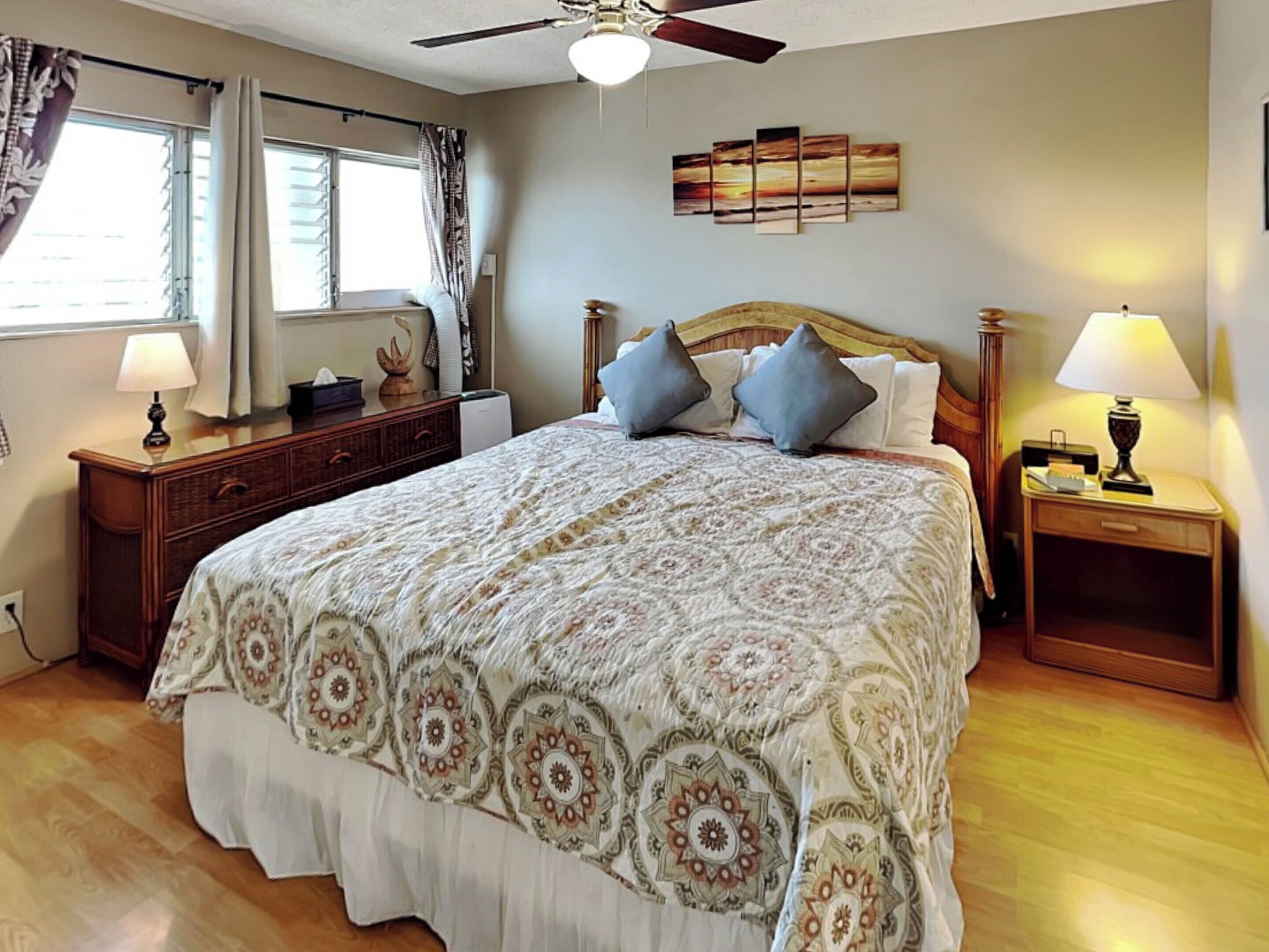 A bedroom with a large bed, two nightstands, a ceiling fan, a window with curtains, and a wall art piece.