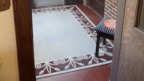 A wooden door with a glass panel, a bench with a cushion, and a patterned mat.