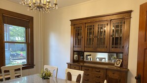 A dining area with a granite table, white chairs, a chandelier, and wooden cabinets with glass doors.