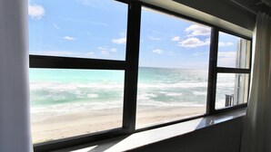 Vista de una playa a través de una ventana, con cielo despejado y océano.