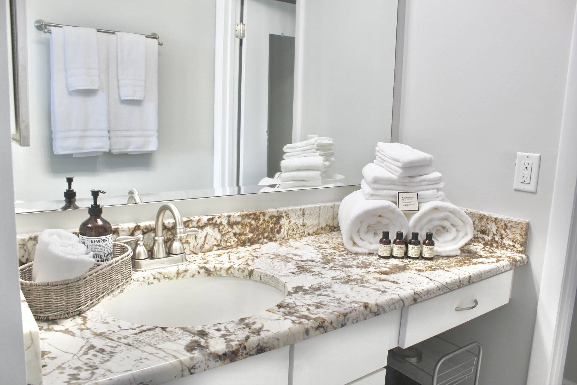 A bathroom with a marble sink, a mirror, a towel rack, and toiletries.