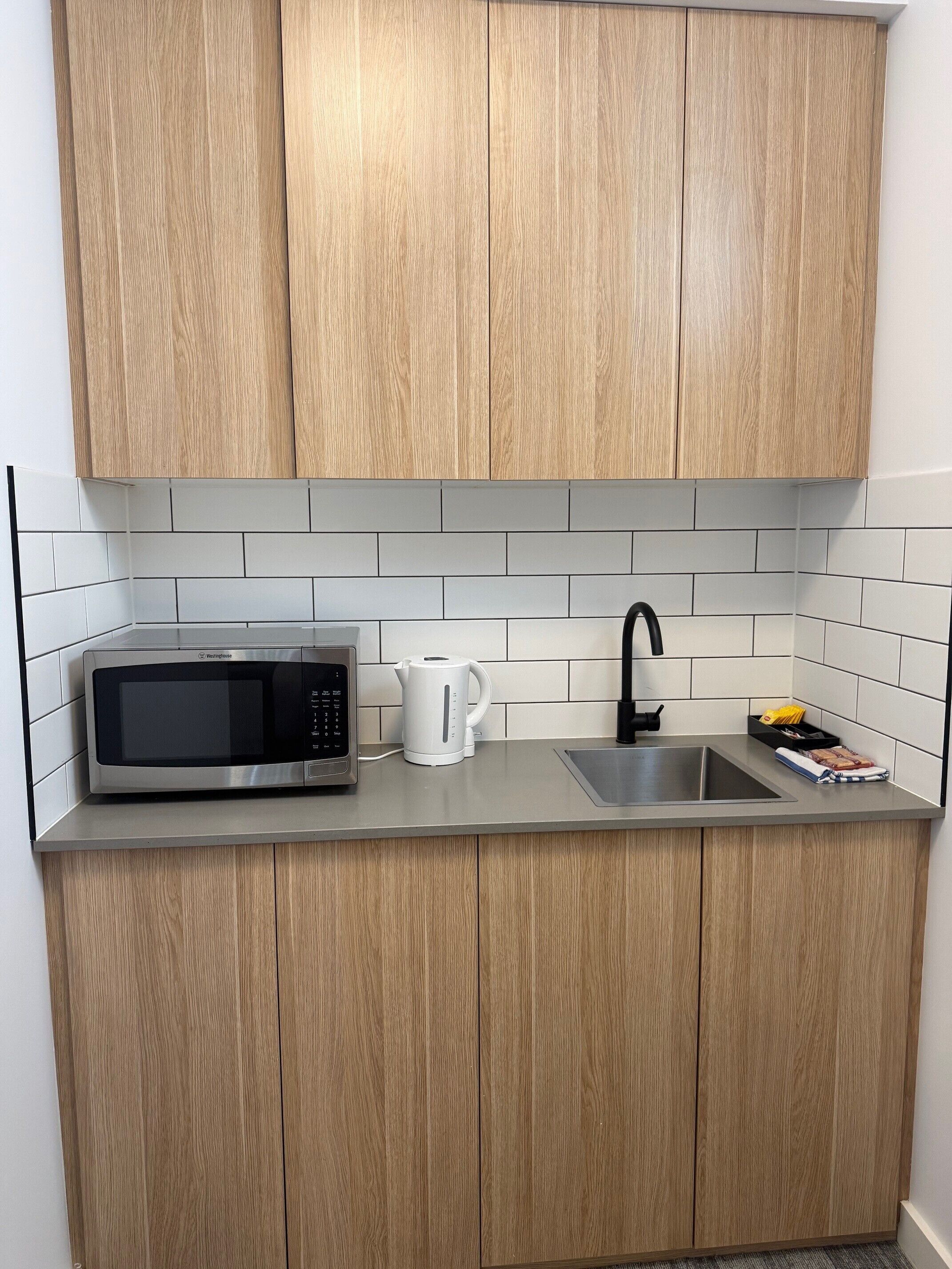 A kitchen with wooden cabinets, a stainless steel countertop, a microwave, a kettle, and a sink.