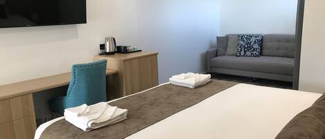 A hotel room with a bed, a desk, a chair, a sofa, and a flat-screen TV.