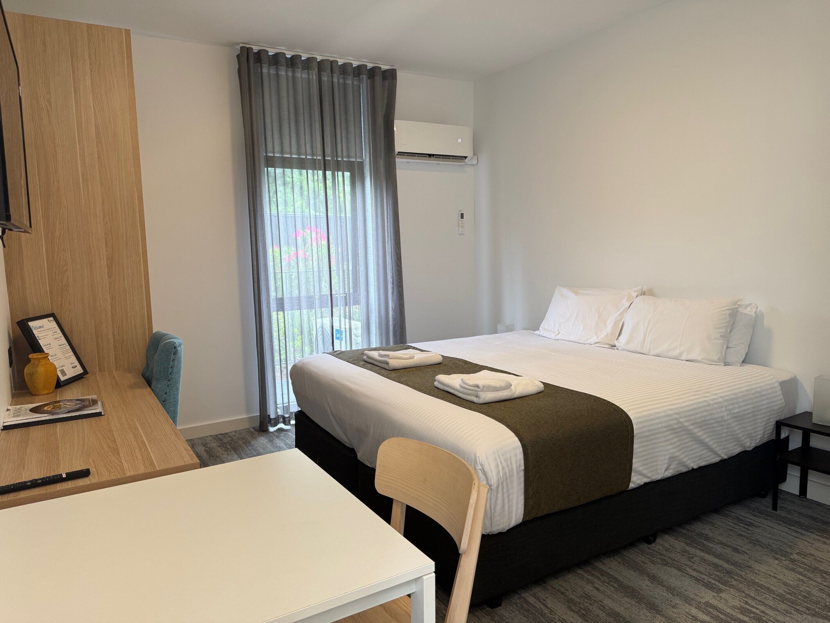 Une chambre d’hôtel avec un lit, un bureau, une chaise, une petite table et une fenêtre avec des rideaux.