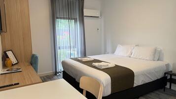 Une chambre d’hôtel avec un lit, un bureau, une chaise, une petite table et une fenêtre avec des rideaux.