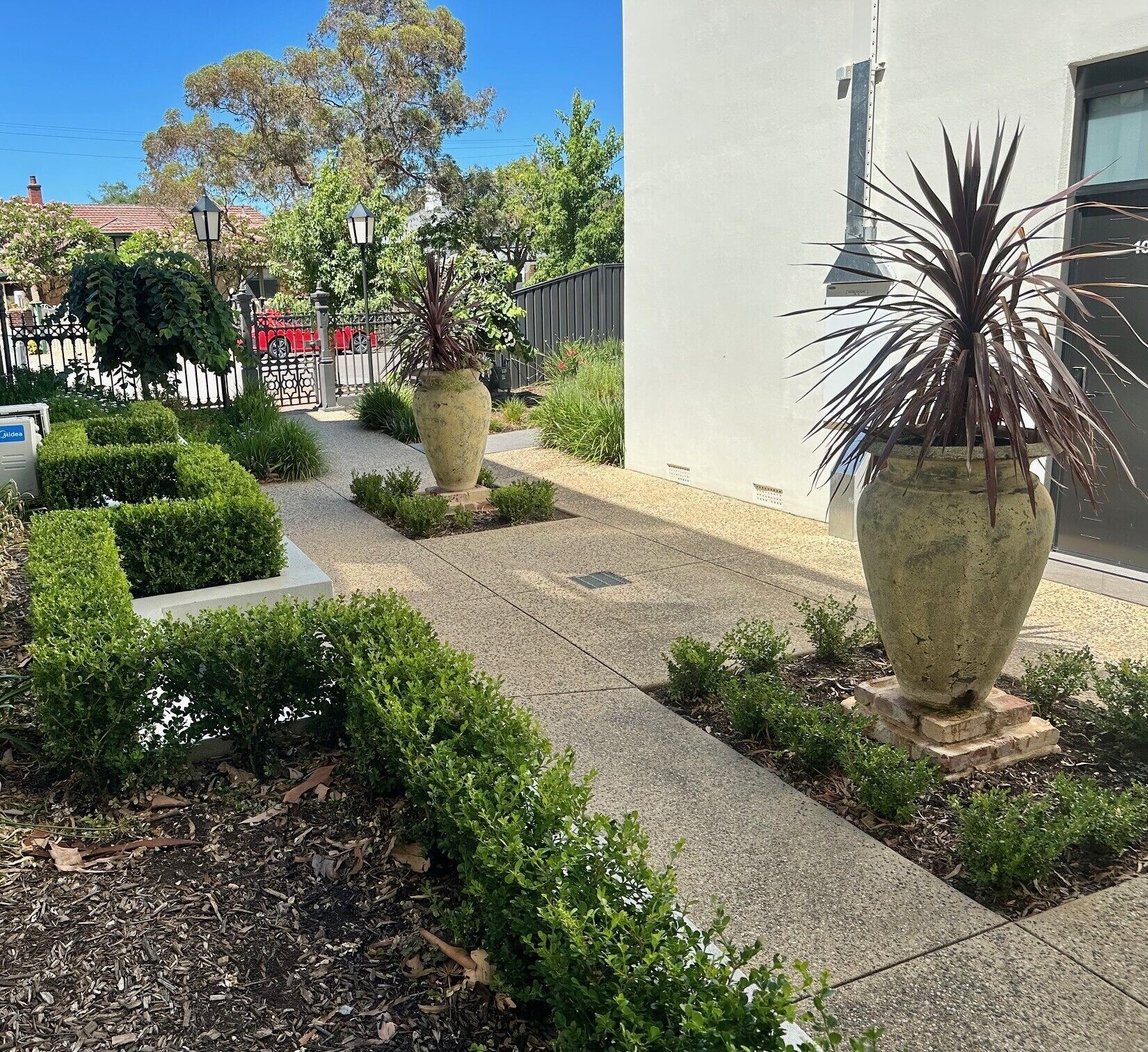 Un sentier aménagé, agrémenté de plantes en pot et de haies taillées.