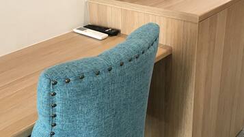 A wooden desk with a blue chair featuring buttoned details. A kettle, a remote control, and a tray with items are on the desk.