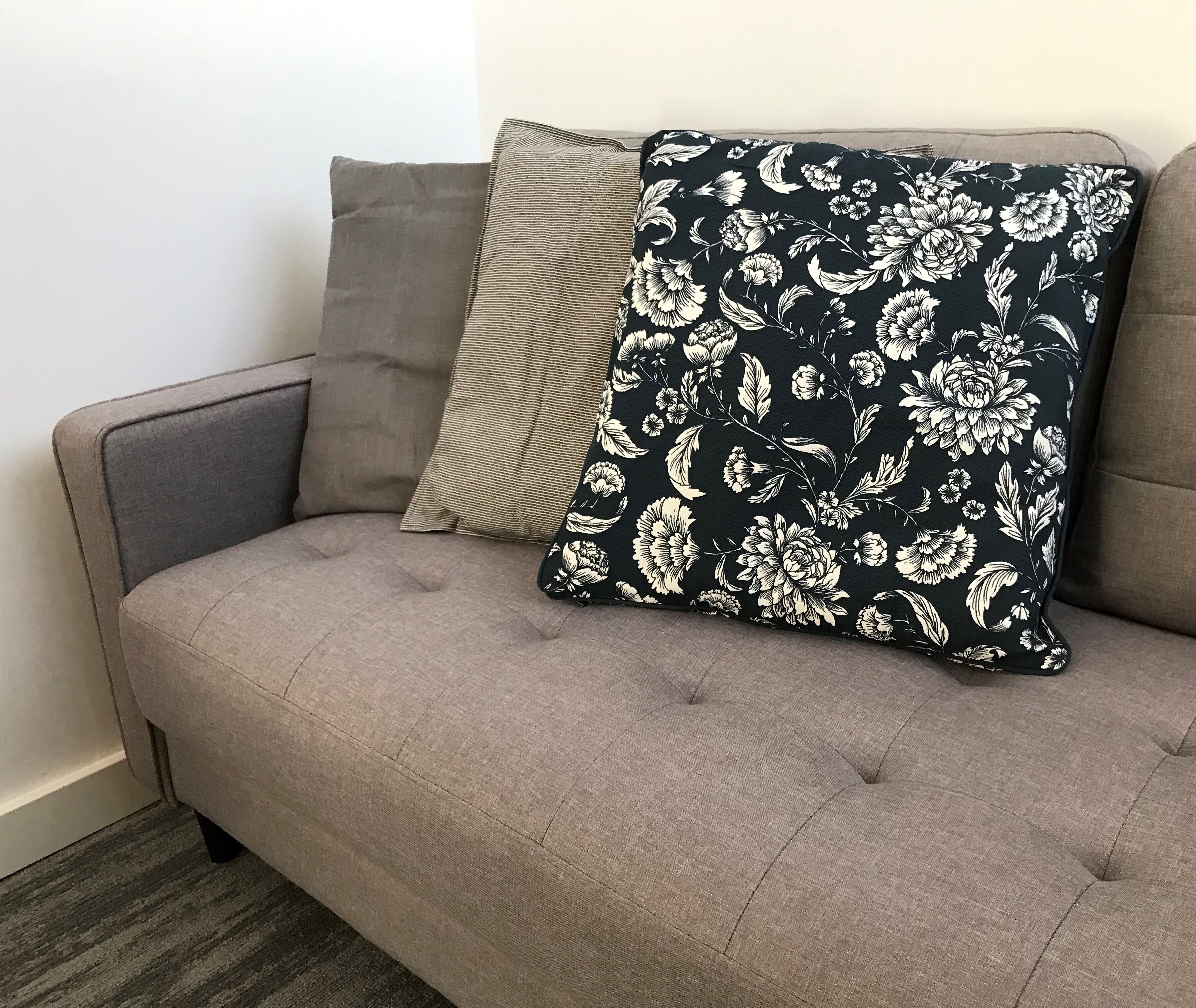 A grey sofa with two pillows, one striped and one with a floral pattern.