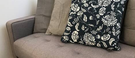 A grey sofa with two pillows, one striped and one with a floral pattern.