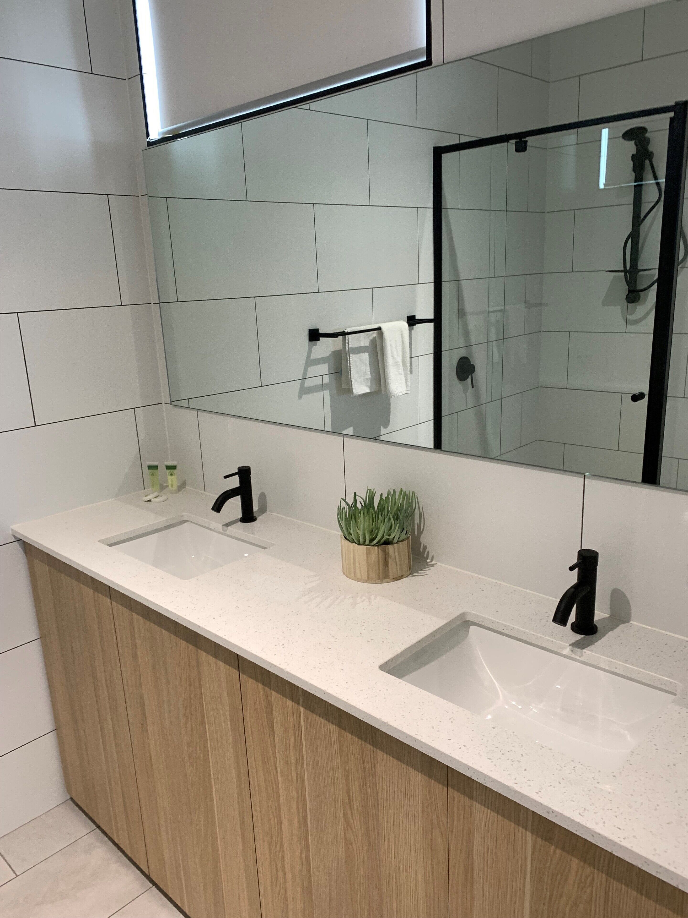 A modern bathroom with a wooden vanity, two sinks, a mirror, and a shower area.