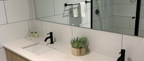 A modern bathroom with a wooden vanity, two sinks, a mirror, and a shower area.