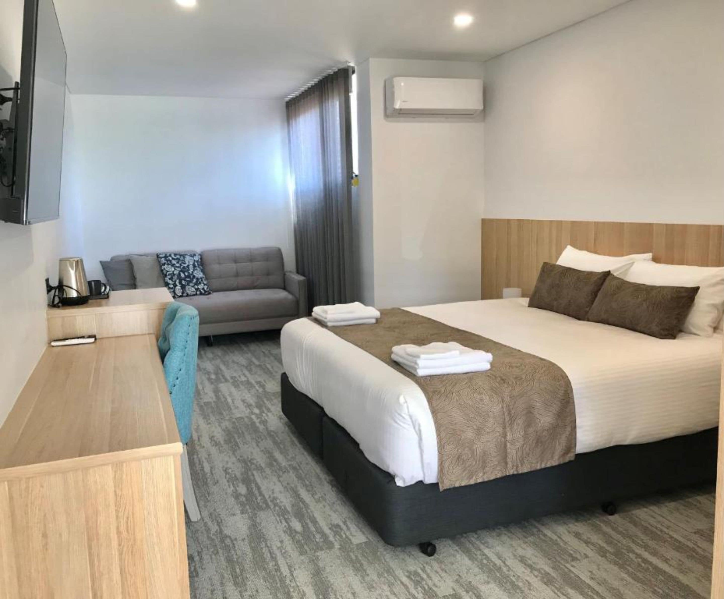 A hotel room with a bed, a sofa, a desk, and a TV.