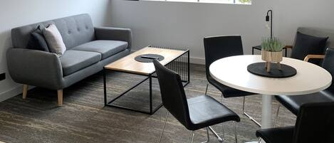 A modern living room with a grey sofa, a round coffee table, and black chairs.