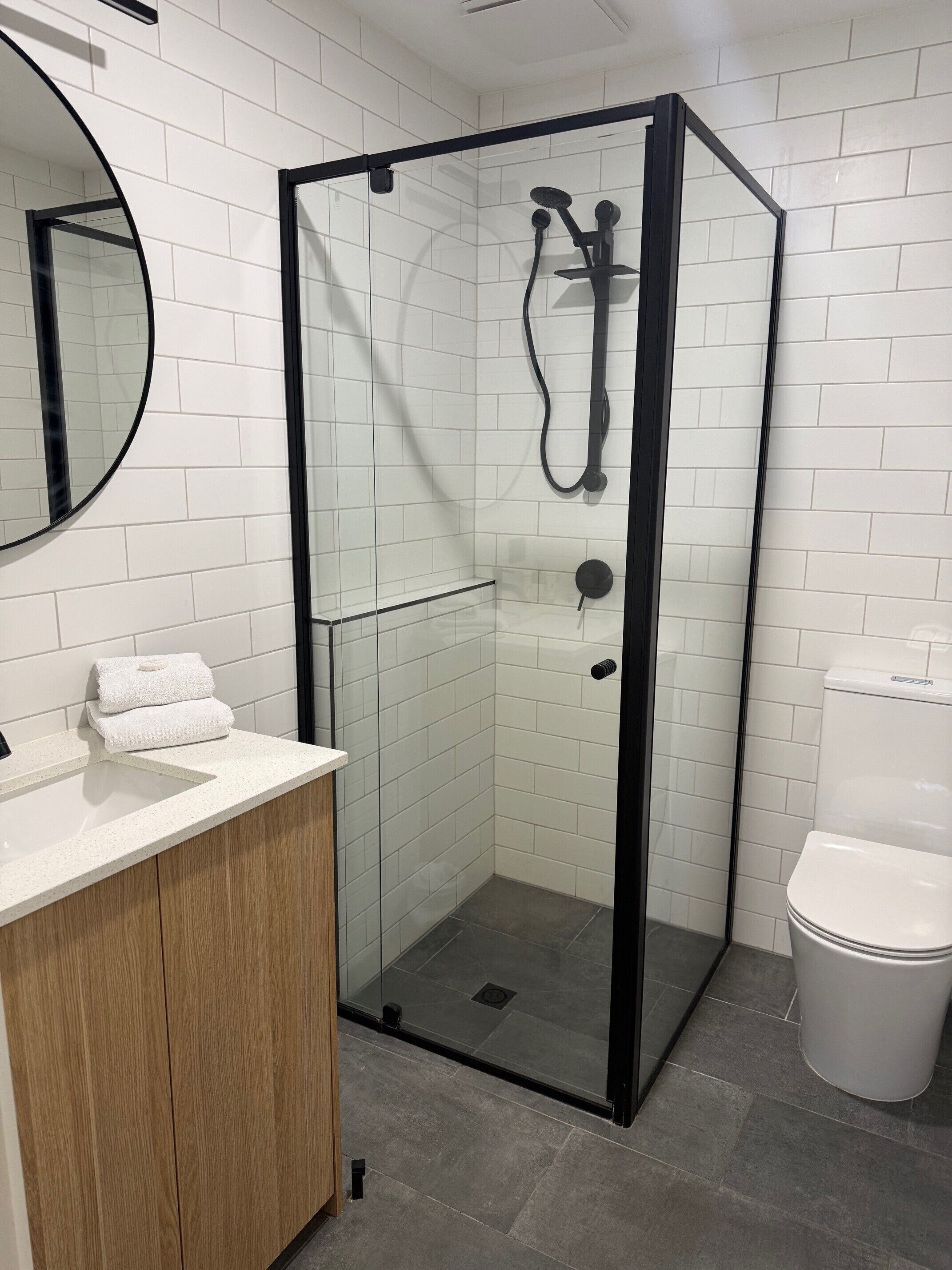 A modern bathroom with a glass-enclosed shower, a wooden vanity, a white sink, and a toilet.