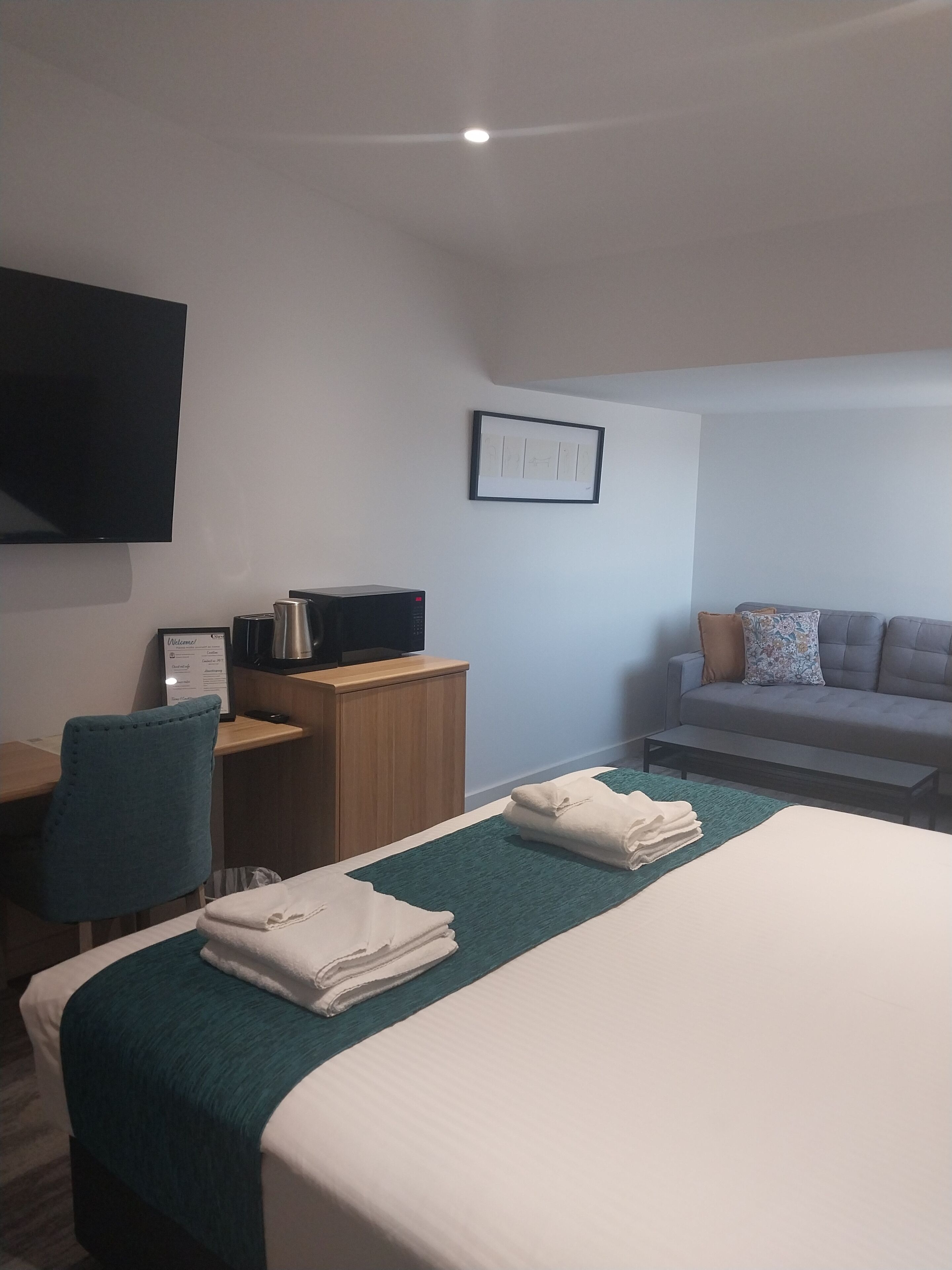 Une chambre d’hôtel équipée d’un lit, d’un bureau, d’une chaise, d’un canapé et d’un téléviseur à écran plat fixé au mur.