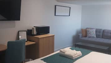 A hotel room with a bed, a desk, a chair, a sofa, and a flat-screen TV mounted on the wall.