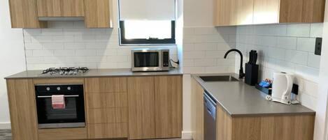A modern kitchen with wooden cabinets, a built-in oven, a microwave, a dishwasher, and a window above the sink.