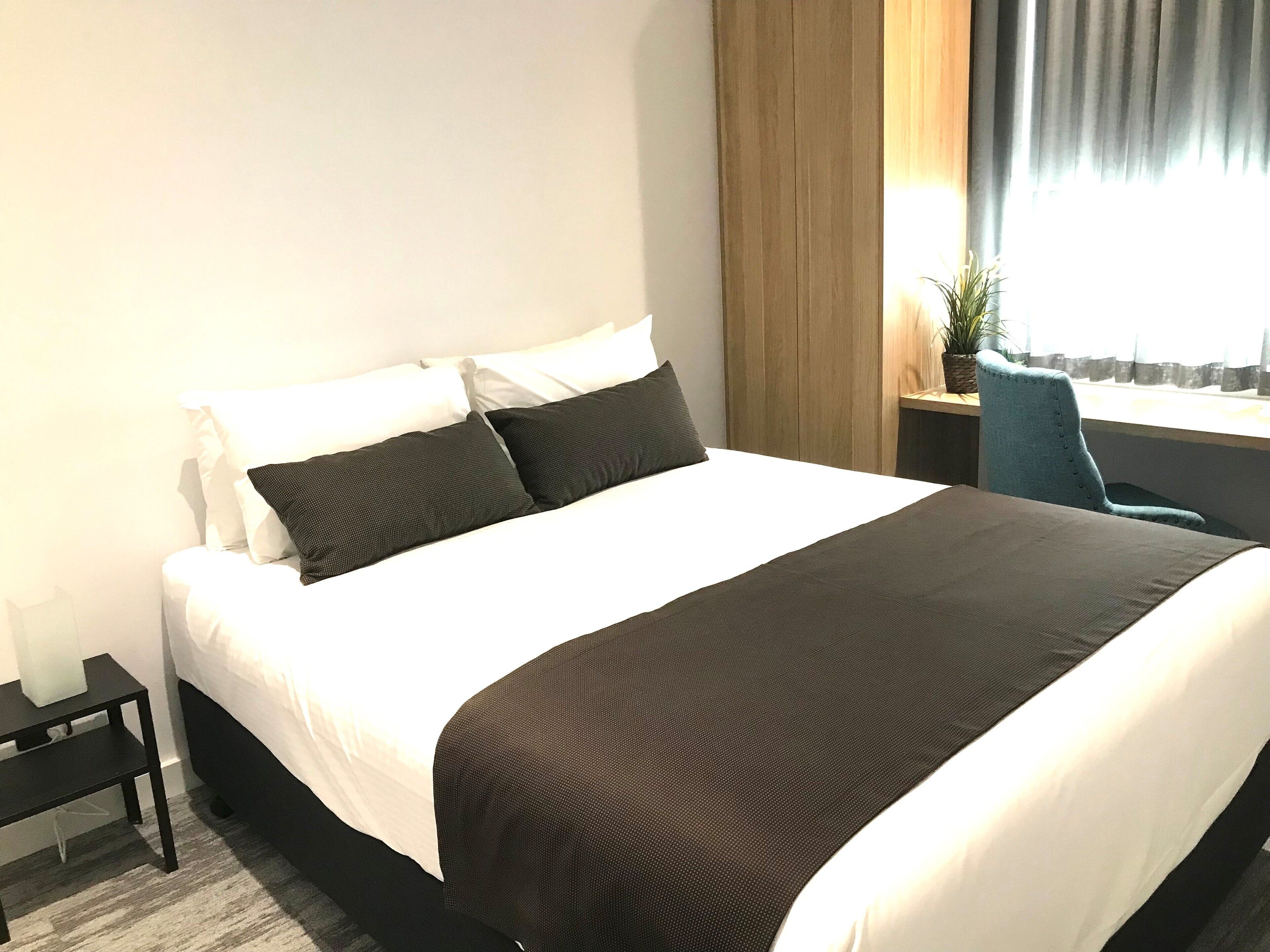 Un letto rifatto con cuscini bianchi e scuri, una coperta marrone scuro e una testiera in legno.