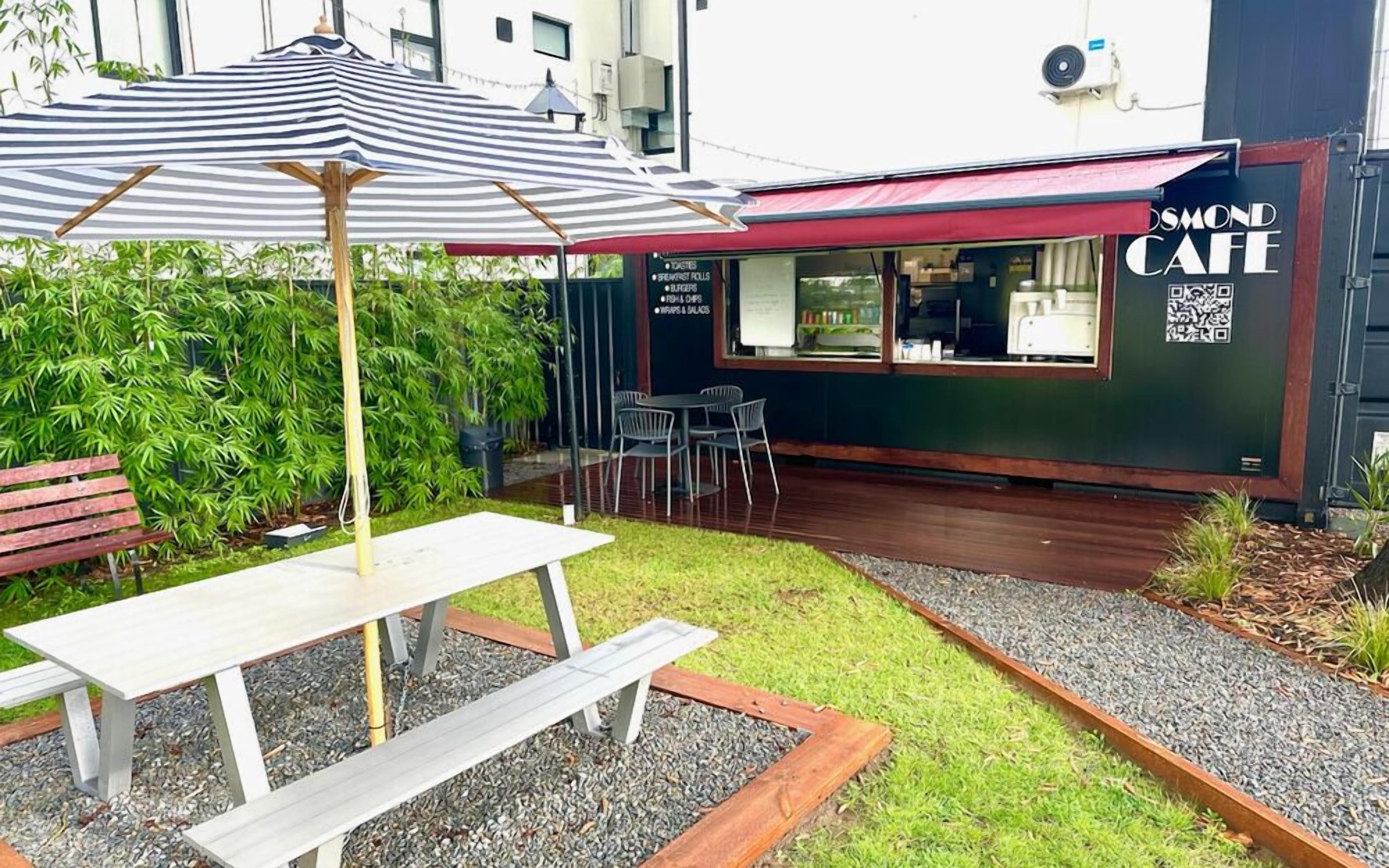 Un espace extérieur aménagé avec une table et des chaises, un parasol à rayures et un panneau affichant le menu devant un café.