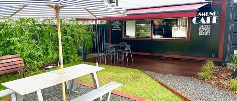 Un espace extérieur aménagé avec une table et des chaises, un parasol à rayures et un panneau affichant le menu devant un café.