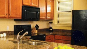 Una cocina con armarios de madera, un microondas negro, un lavamanos y un bol de limones en la encimera.