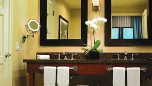 Un baño con dos lavamanos, un espejo grande, un espejo redondo pequeño y una orquídea en maceta.