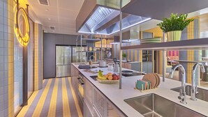 Une cuisine moderne dotée d’appareils électroménagers en acier inoxydable, d’un îlot central agrémenté de fruits et d’ustensiles de cuisine, et d’une plante en pot posée sur le plan de travail.