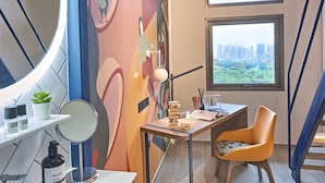 Une salle de bain moderne avec un grand miroir, un lavabo et une chaise. Il y a des fenêtres donnant sur la ville, et une fresque colorée sur le mur.