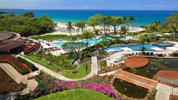 Een resort met meerdere zwembaden, een strand en een groot gebouw met een gebogen dak.