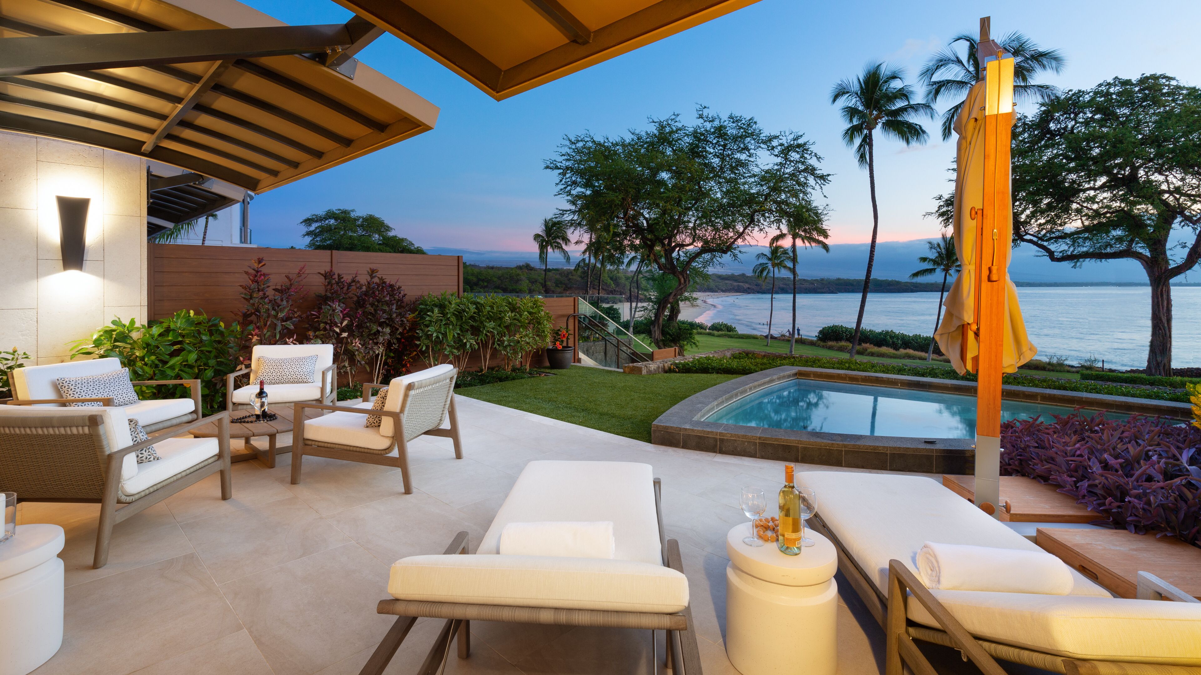 A poolside area with lounge chairs, a hot tub, and a view of the ocean at sunset.