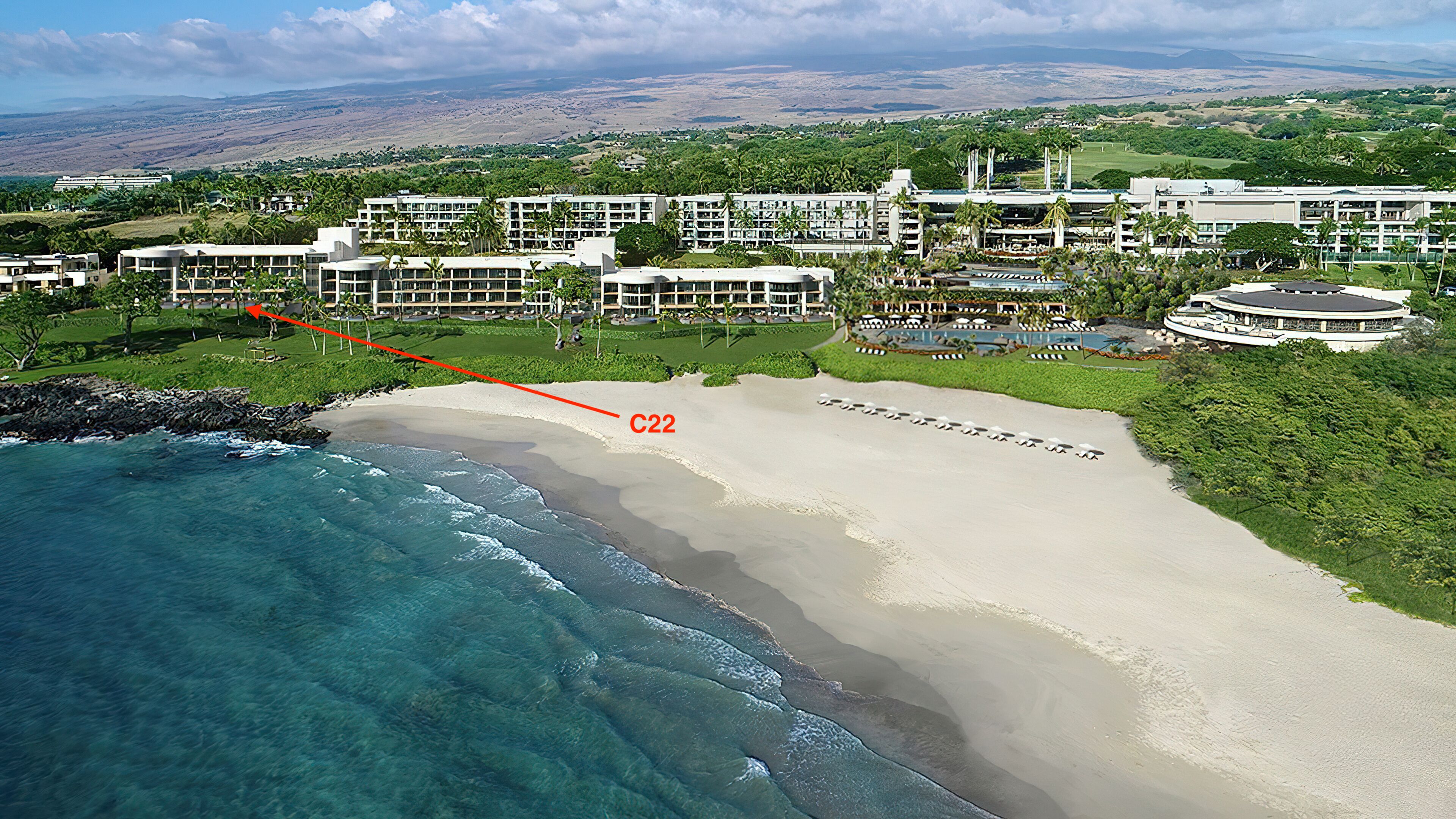 An aerial view of a resort with a beachfront, including a sandy beach, clear blue waters, and lush greenery.