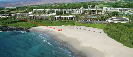 An aerial view of a resort with a beachfront, including a sandy beach, clear blue waters, and lush greenery.