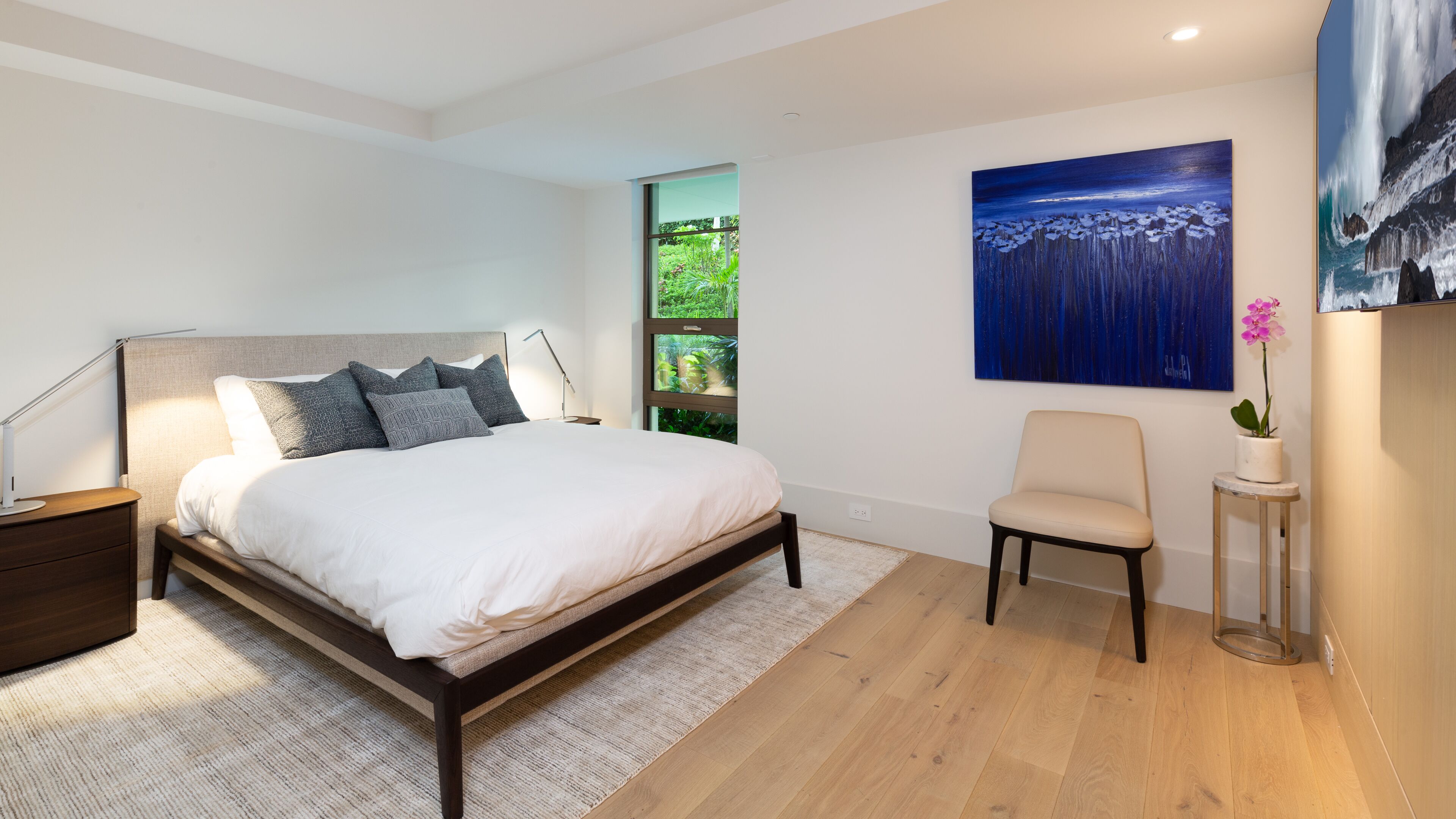 Un dormitorio moderno con una cama grande, una mesita de noche, una silla y un cuadro en la pared.