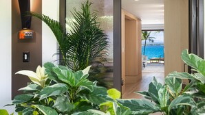Een moderne hotelgang met een grote potplant, een bord met het cijfer C22, en uitzicht op een balkon met een zwembad en palmbomen.