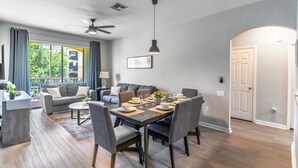 A modern living room with a dining area, grey sofas, a wooden dining table, and a ceiling fan.