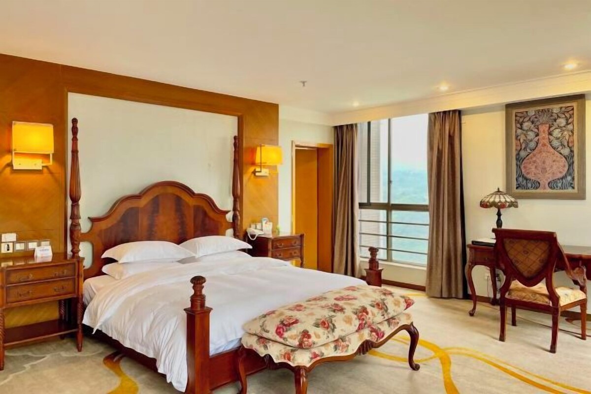 A hotel room with a large bed, bedside tables, a desk, and a chair.