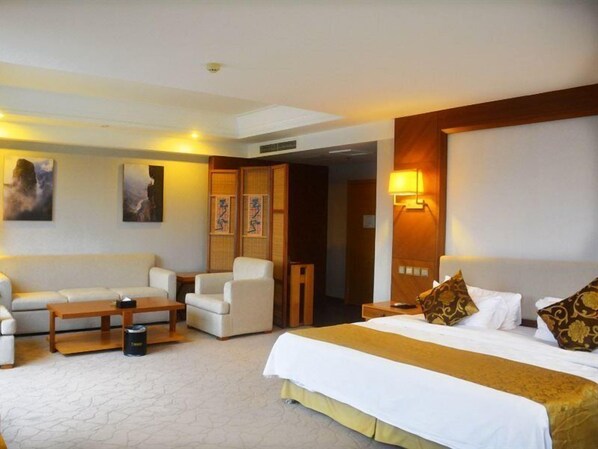 Habitación de hotel con una cama grande, un sofá, una silla y una mesita. Hay lámparas de pared y obras de arte en las paredes.