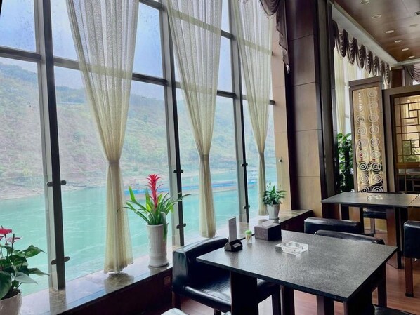 A restaurant with large windows, a table, chairs, and potted plants. - Purple Light Hotel (Zhaotong)