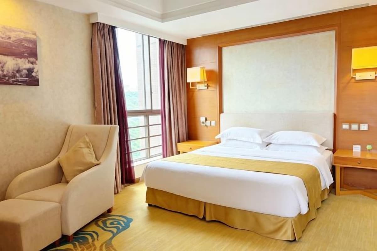 Une chambre d’hôtel avec un lit, une chaise, une table de chevet et une fenêtre avec des rideaux.