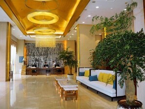 Un vestíbulo amplio con mostrador de recepción, un sofá grande con cojines, una mesa de centro y una planta grande en maceta.