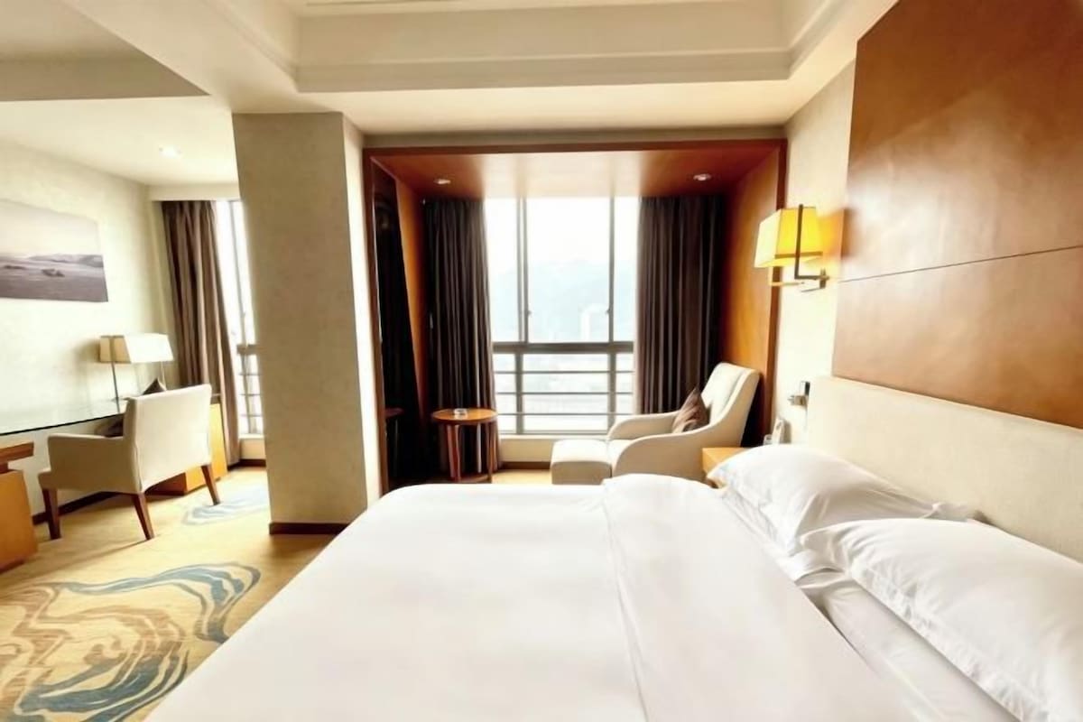 Une chambre d’hôtel avec un grand lit, un bureau, une chaise et une vue sur la ville.
