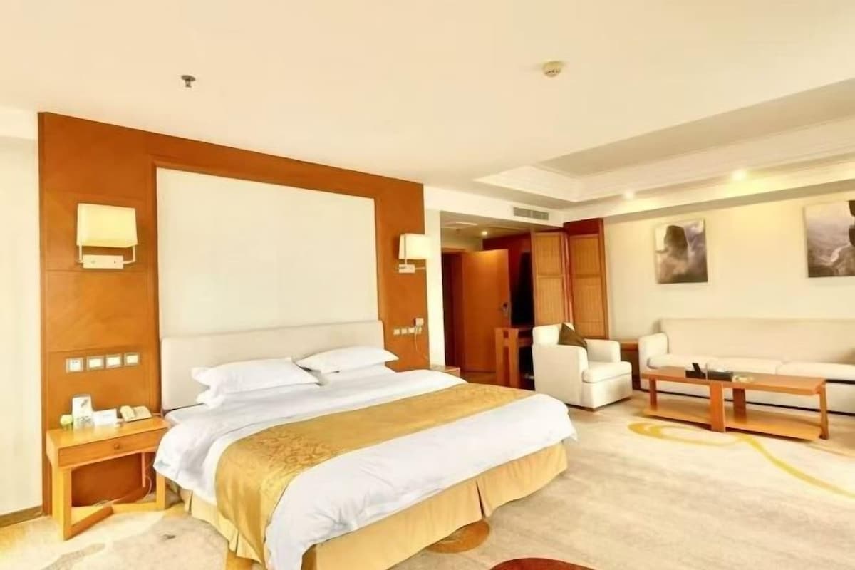 Une chambre d’hôtel dotée d’un grand lit, de tables de chevet, d’un coin salon avec un canapé et des fauteuils, et offrant une vue sur la ville.