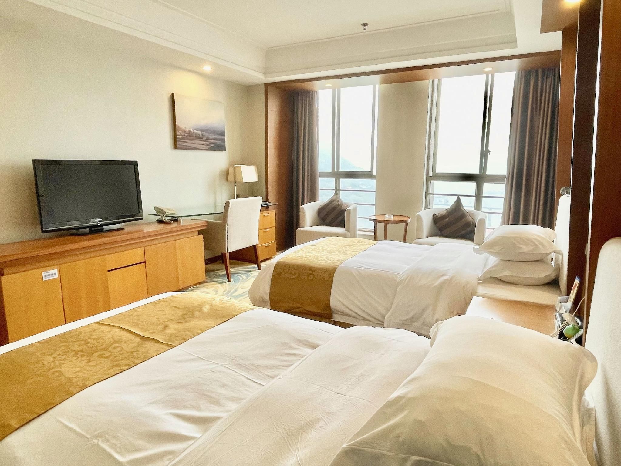 A hotel room with a television, a desk, two beds, a chair, and a view of the outdoors.