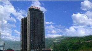 Um hotel alto com vários andares, situado perto de um rio, com vista para colinas verdes ao fundo.