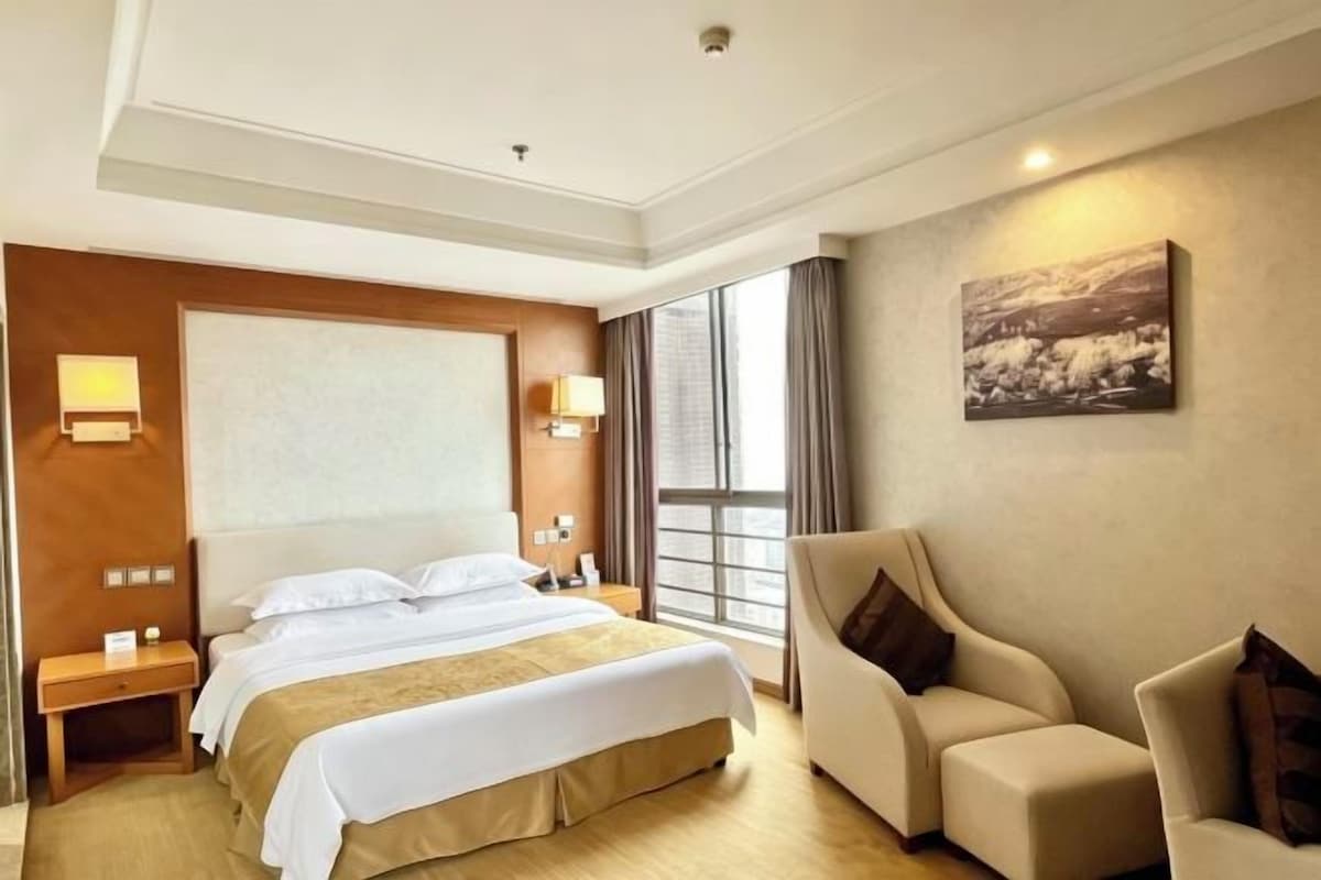 A hotel room with a large bed, a sofa, a nightstand, and a painting on the wall.