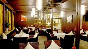 Restaurante com interiores em madeira, mesas com toalhas brancas e luminárias pendentes.