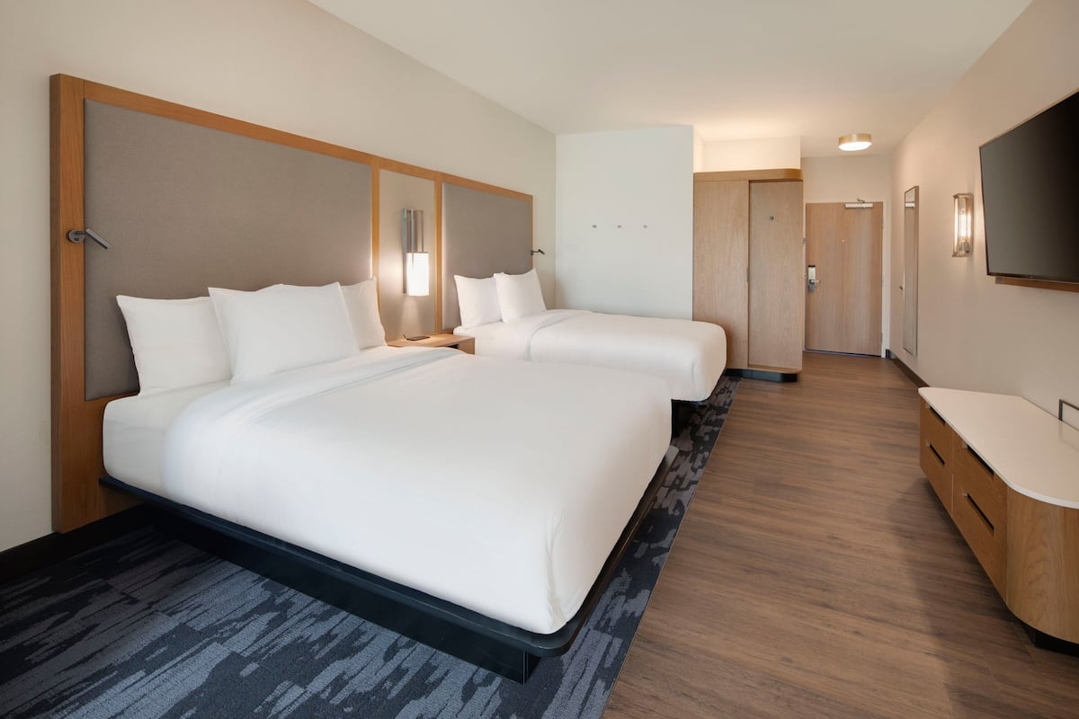 Habitación de hotel con dos camas, un cabecero de madera, un televisor de pantalla plana y un mueble de madera.